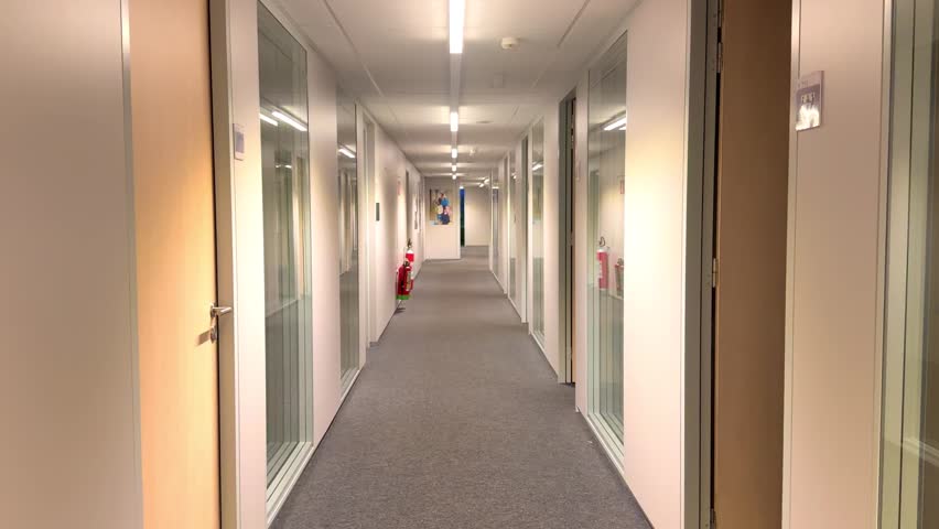 Smooth POV walk-through of a modern, empty office corridor. First-person perspective moving along a hallway with glass doors in a corporate building.
