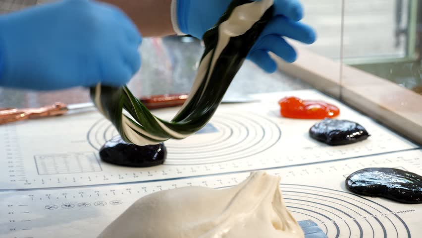 Close-up of a pastry chef wearing gloves as he mixes liquid caramel with his hands on a table in a pastry shop, producing caramel candies in different colors.