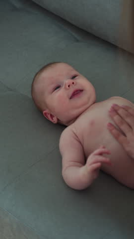 Close-up of adorable newborn baby with blue eyes lying on a soft grey couch, looking curious and alert