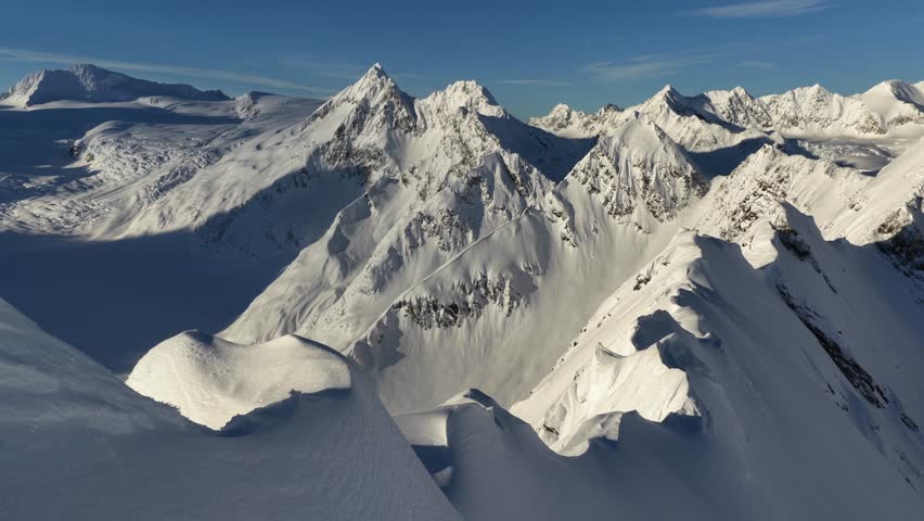 Aerial view of sunlight dancing on the pristine, snow-covered peaks, carving stark shadows across the majestic mountain range, Anchorage, Alaska, United States.