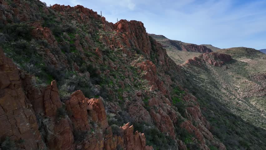 Aerial view of steep, rocky mountains with sparse green vegetation creating a textured landscape under a partly cloudy sky, Morristown, Arizona, United States.