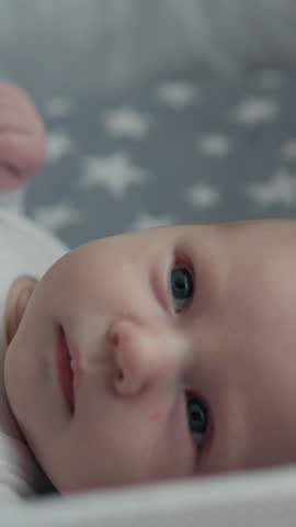 Newborn infant looking upwards with curious blue eyes, lying on soft bedding with star pattern