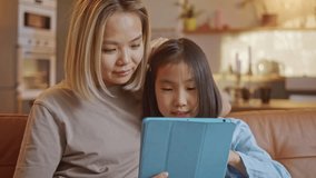 A young woman and her child sit on a sofa and interact with a digital tablet using a stylus in a warm, cozy home interior. The mother guides the girl through educational apps, drawing, or online - Powered by Shutterstock - Get 15% off with code: PIKWIZARD15