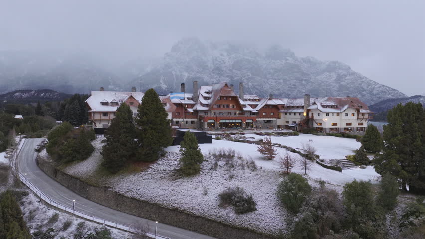 Aerial reveal of Llao Llao hotel in Bariloche surrounded by snow mountains and lake in Patagonia winter.