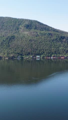 Portrait drone view across Grand Lake Colorado showing the lakefront village, mountain backdrop, wooded neighborhoods, and shoreline development in a picturesque summer landscape