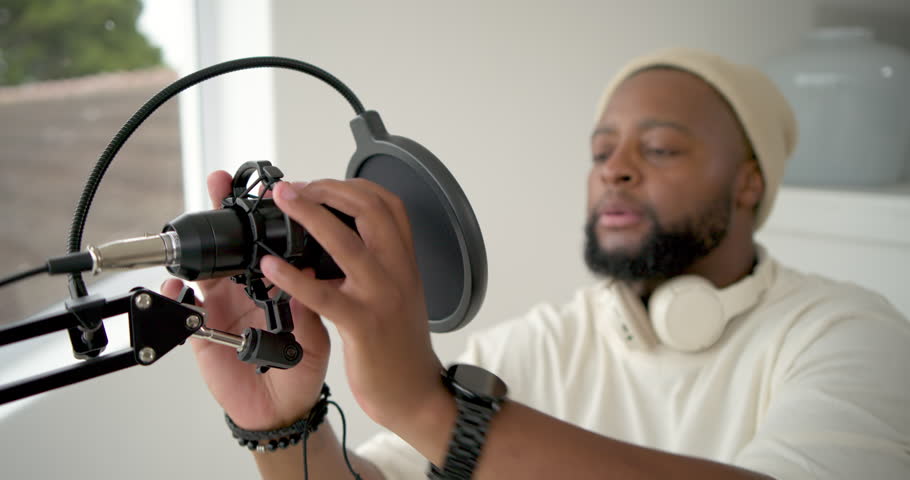 Man adjusting mic pop-filter mount lifting headset preparing to record in home studio, copy space. Podcast, voiceover, microphone, condenser, studio, daylight, window
