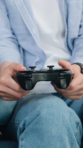 Two different ages female players in blue shirts and jeans sitting on comfortable sofa at home and playing video games using joysticks slow motion