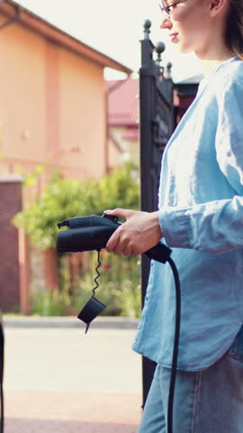 Close up view of a woman that pulls out the charger of an electric car. Plugged charging cable electric vehicle, EV parking, power charger cable, charging port station, sustainable future. Slow motion