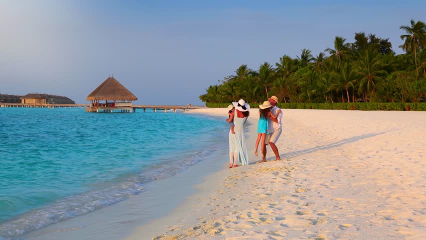 A happy holiday family is having fun on a tropical beach in the Maldives islands during sunset time