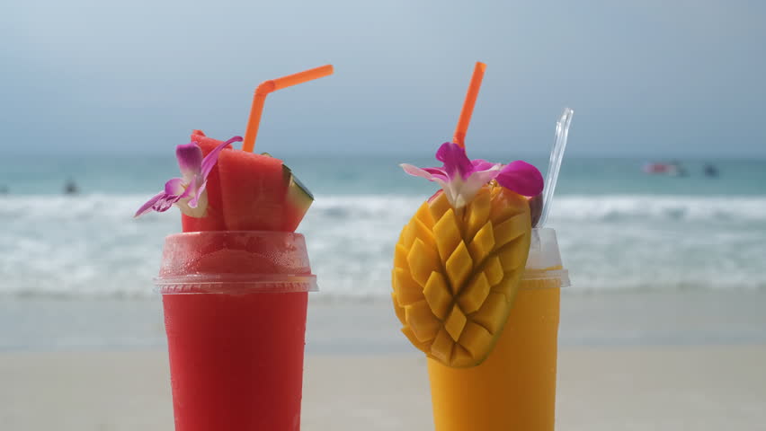 Two vibrant tropical smoothies made from fresh mango and watermelon served with straws and fruit garnish on a sunny beach table. Tropical refreshment concept