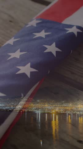 Vertical video: Close crop starting camera pan revealing folded US flag and skyline honoring vets. Ensign, patriotic, commemorative, solemn, cinematic, moody, vertical video