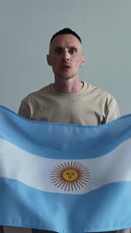 An enthusiastic emotional Argentine sports fan holding the Argentine national flag screaming with joy and celebrating a goal while watching a football match