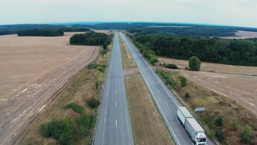 Cars drive on one lane of long road stretching between trees