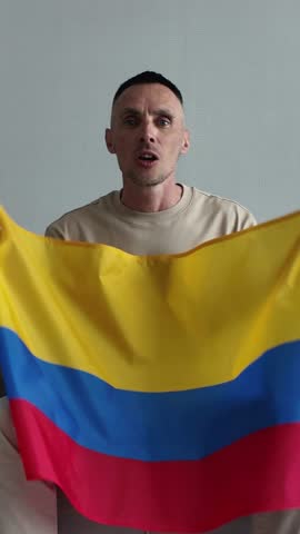 An enthusiastic emotional Colombian sports fan holding the Colombian national flag screaming with joy and celebrating a goal while watching a football match