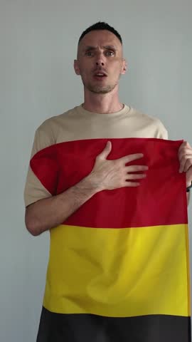 A patriotic man proudly sings the Belgian national anthem while holding the Belgian flag. An emotional sports fan cheers for his national team