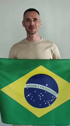 A happy man holds a Brazilian flag. An enthusiastic fan cheers for his favorite national team