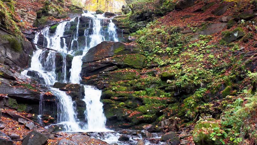Narrow stream falling down mountain slope in autumn forest