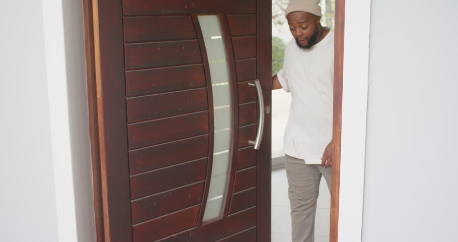 Adult male approaching and opening wooden door, inspecting cardboard box and retrieving delivery. Parcel, home, minimalist, residential, porch, candid, natural