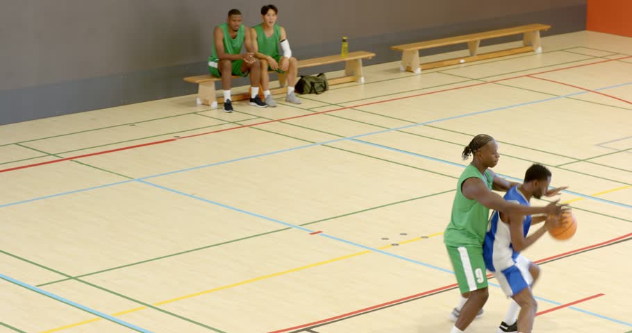Defender pressuring African American male faking drive and crossing over ball on gym court for shot. Athletics, competition, training, technical, determination, teamwork, action