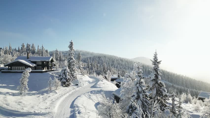 Aerial glide past misty mountain cabins in fresh snowfall and golden morning light, Valdres, Norway.