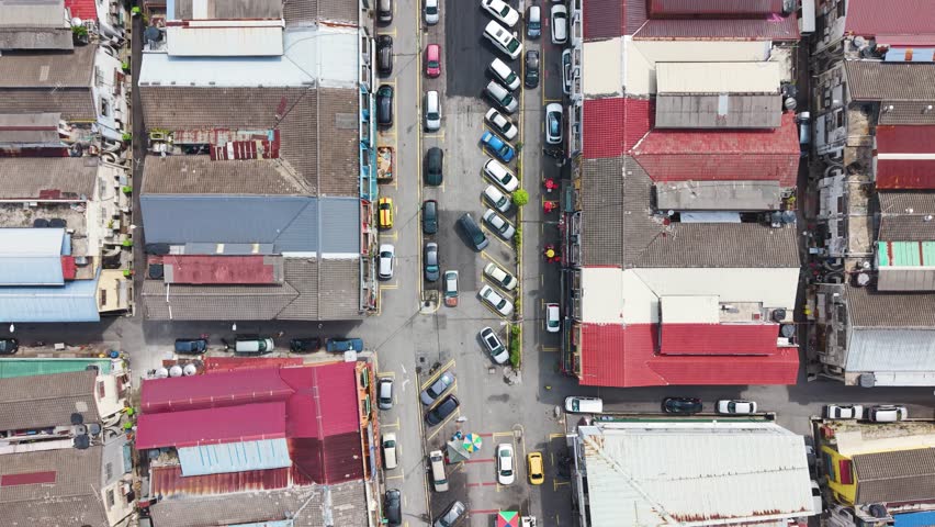 Top-down aerial view of parked cars in Cheras district in Kuala Lumpur, Malaysia. Dense urban layout with colorful rooftops, street activity, and a local commercial area.