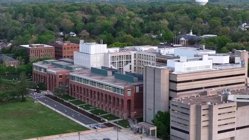 Aerial view of Fairfax County Government Center in Fairfax, Virginia, with large brick administrative buildings, surrounding greenery and roads. Soft evening light in spring season. Orbit shot.