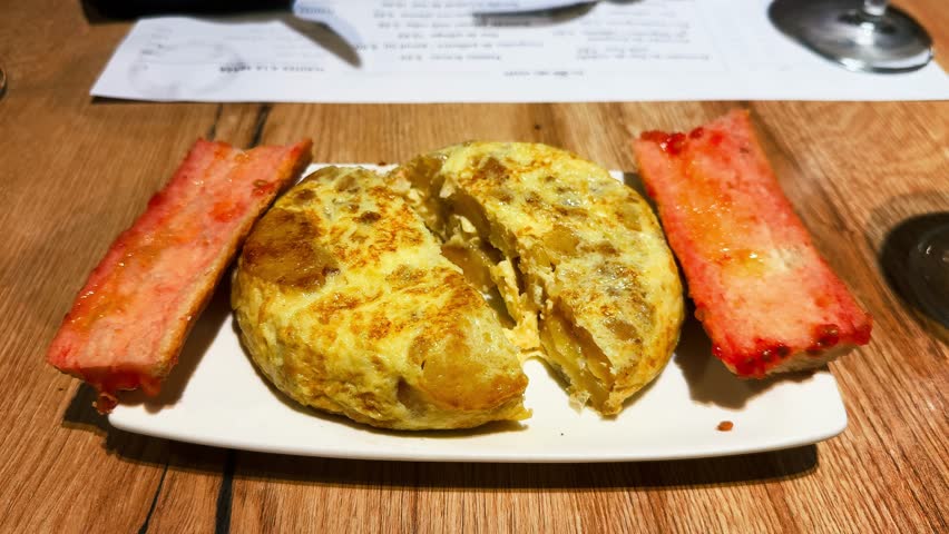 Pan con tomate and tortilla served on a plate. In a cozy restaurant setting, a person gently cuts into the tortilla, revealing its soft, tender center. High quality 4k footage