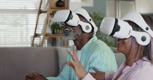 Senior couple being prompted by white VR headsets both pointing and choosing virtual items on sofa. Goggles, pair, elderly, home, livingroom, cozy, candid - Powered by Shutterstock - Get 15% off with code: PIKWIZARD15