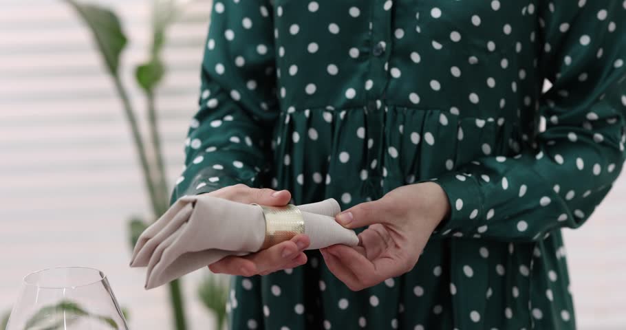 Beautiful place setting. Woman folding napkin with ring at table indoors, closeup. Camera moving down and backwards