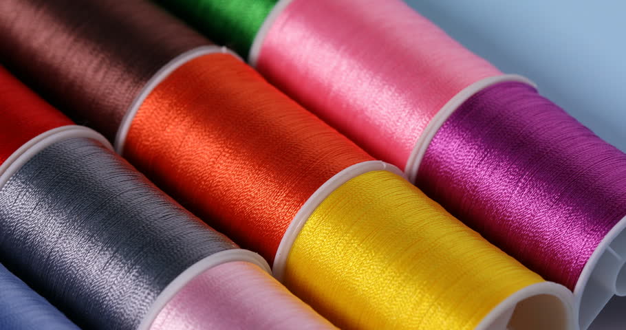 Spools of sewing threads on light blue background, closeup. Camera moving left