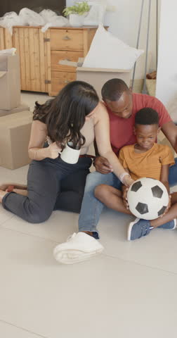 Playing family of three passing black-and-white soccer ball on tiled floor at home, with boxes. Parents, child, mug, orb, unpacked, livingroom, vertical video