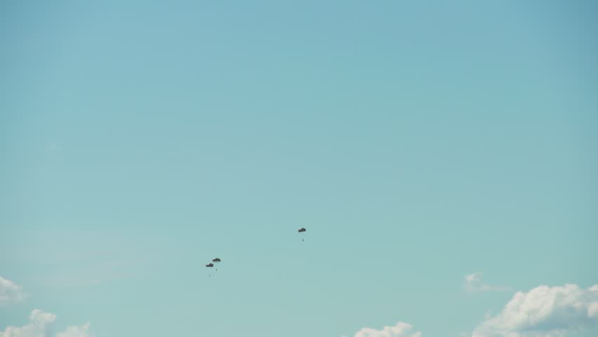 Paratroopers descending over forest landscape beneath blue sky during airborne training