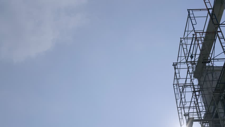 Looking up at a metal scaffolding framework installed on the exterior of an unfinished concrete building. Construction site and real estate development concept against a clear blue sky background with copy space.