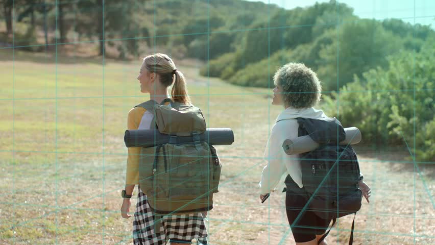 Two women hikers starting hike across meadow with packs and mats, heading toward treeline travel. Backpacks, hiking, trail, outdoors, nature, companions, sunny