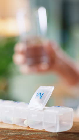 Pills, container and hands with water in home for healthcare supplements, vitamins or minerals. Person, glass and box for pharmaceutical product, drugs and wellness with dosage schedule at apartment