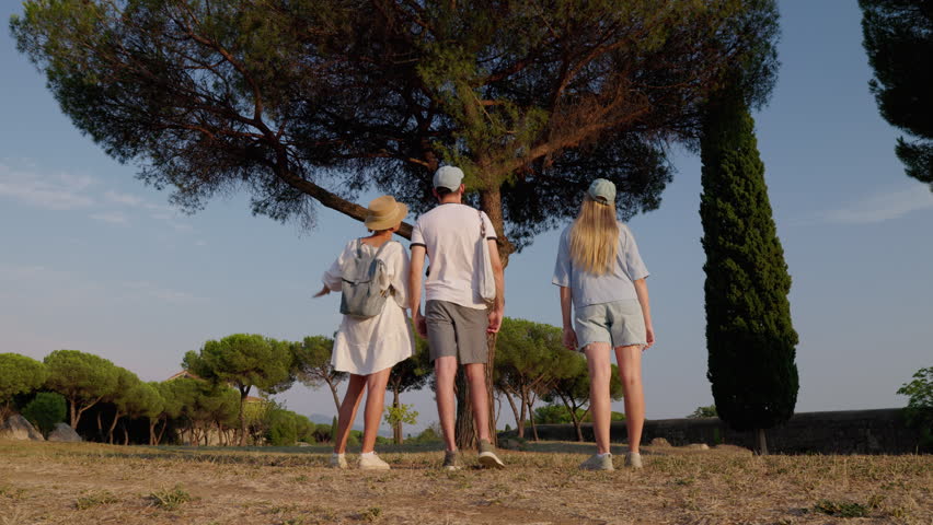 Family standing under pine tree in Appia Antica Park Rome enjoying summer evening light and ancient landscape.