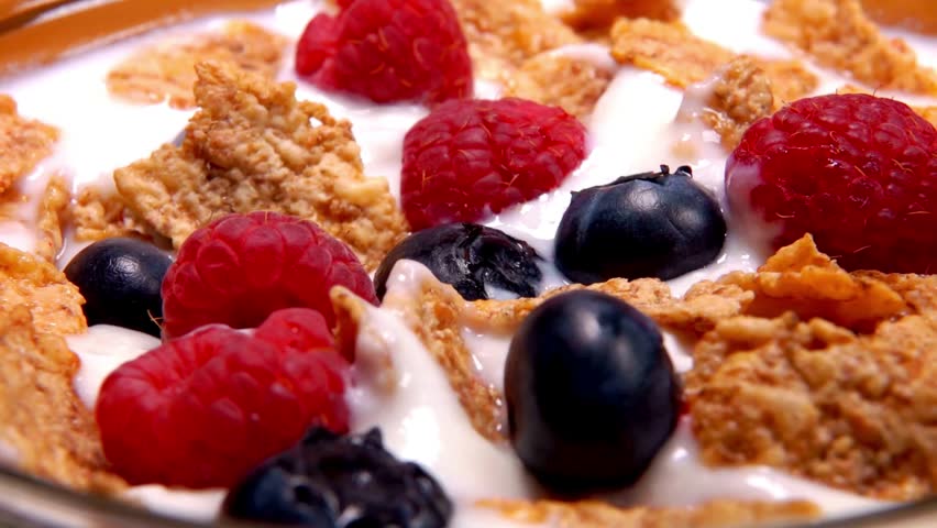 cereals with fruit and milk, closeup. Pouring milk into bowl of cereal, strawberries and blueberries. Milk being poured onto the corn flakes cereal.
