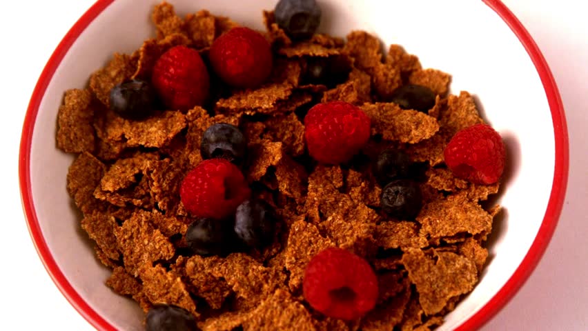 cereals with fruit and milk, closeup. Pouring milk into bowl of cereal, strawberries and blueberries. Milk being poured onto the corn flakes cereal.
