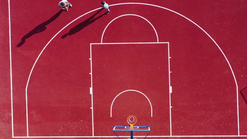 Top aerial view of red outdoor basketball court at school or park playground. Aerial shot of unrecognizable kids playing basketball. view of basketball court.