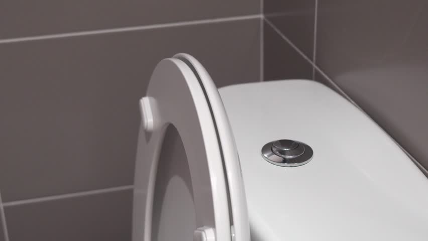 Closeup of male hand pushing a button to flush a close tool a bathroom toilet.