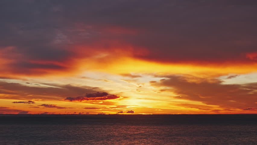 Landscape after sunset with vibrant red and orange sky reflecting on water and shore. Beautiful seascape time lapse, 4k