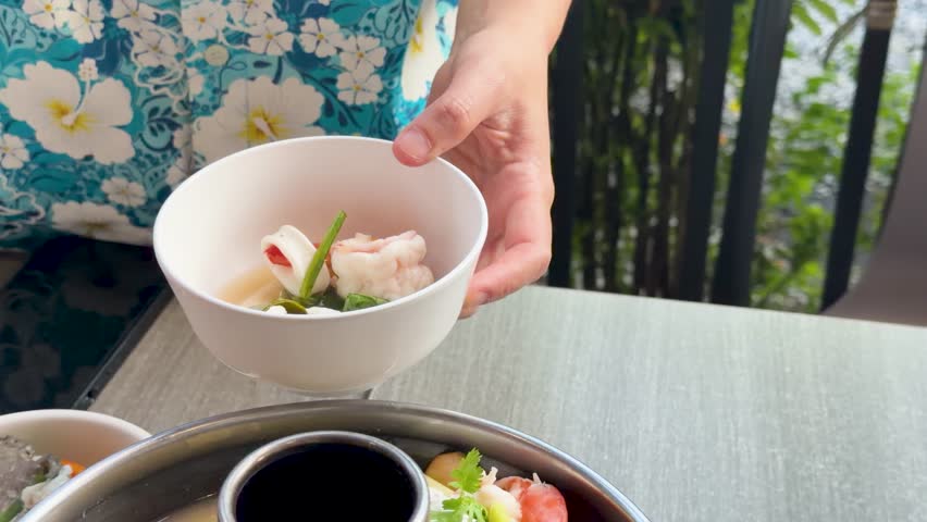 Close-up shot of hands using a ladle to serve hot seafood soup into a bowl