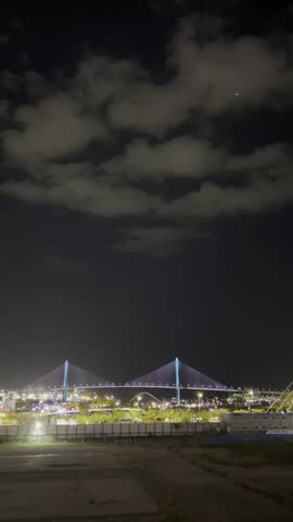 Illuminated cable-stayed bridges and city lights glow against a cloudy night sky in Busan, South Korea.