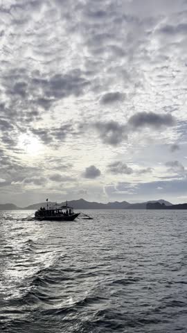 Traditional bangka boat crossing the water in Bacuit Bay near El Nido under a cloudy sky.