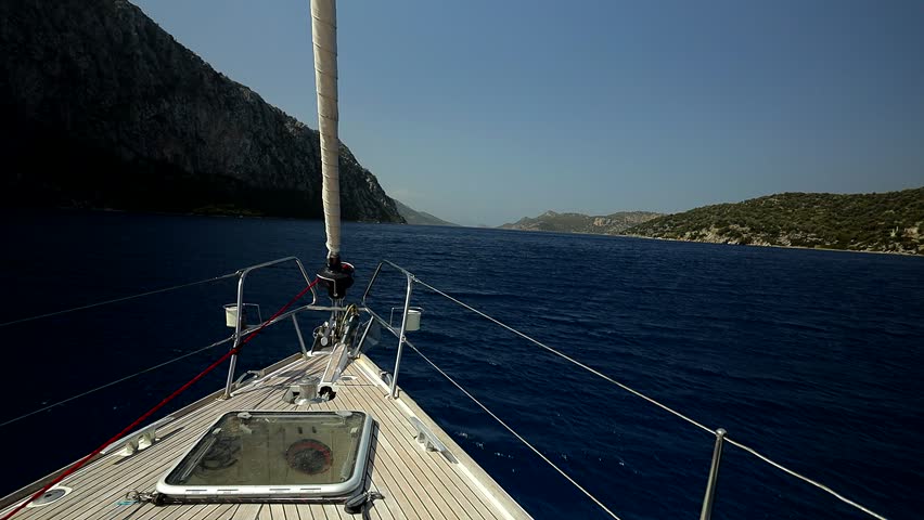 Bowsprit and hatch in the deck of a sailing yacht sailing in a narrow strait between rocky shores
