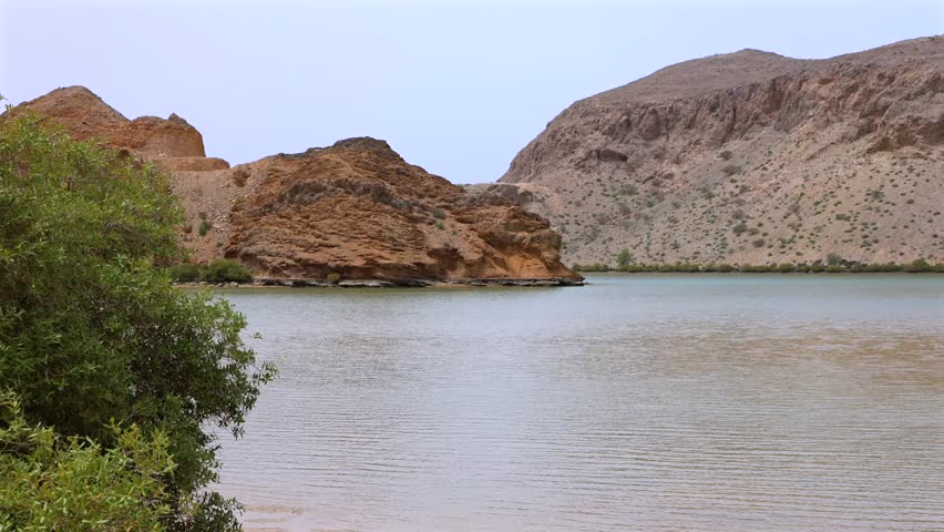 Serene Rocky Landscape. Peaceful Lagoon Amid Stone Hills. Tranquil Water Body Surrounded By Rugged Rocks. Calm Shallow Basin Beneath Muted Sky With Rocky Terrain