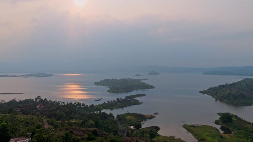 Serene tropical lake scenery with small islands and lush hills under hazy twilight sky