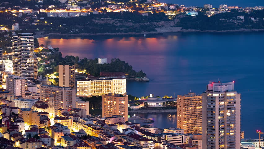 Night timelapse of Monaco Larvotto district with Monte-Carlo Bay Hotel and Sporting complex, glowing city lights, coastal reflections, and dynamic urban motion on Mediterranean shoreline.