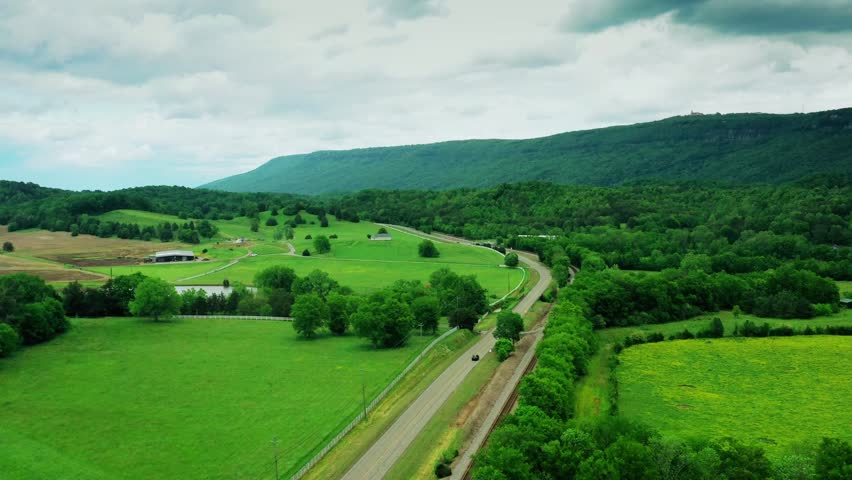 Aerial landscape of mountain forest with scattered houses and linking main roads, dense trees, cloudy daylight sky, scenic rural environment, natural greenery blending with transportation network, peaceful countryside, cinematic view.
