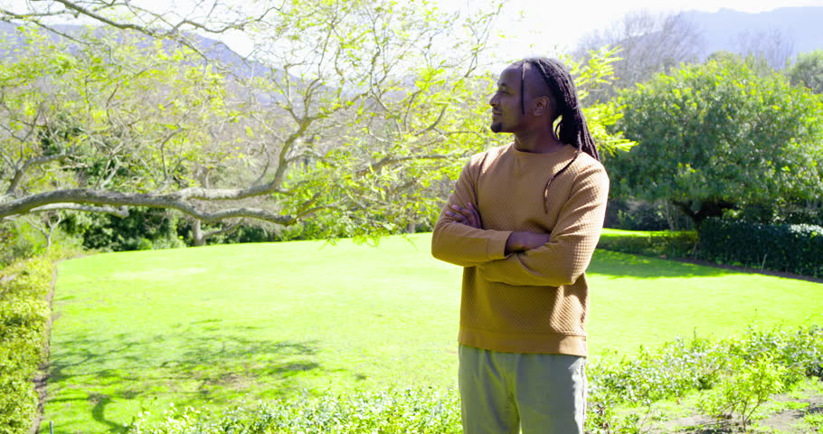 African American man arms crossed yard seeing camera zooming in turning head, smiling, copy space. Outdoors, nature, portrait, relaxation, happiness, lifestyle, casual